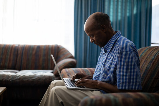 Elderly man using laptop at home, concentrating on work in living room, copy space