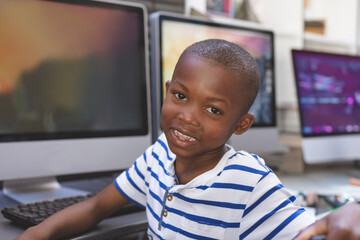 In school, smiling boy in striped shirt sitting at computer desk