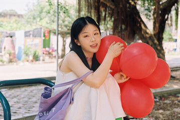 Young woman with red balloons in outdoor park setting exuding joy.