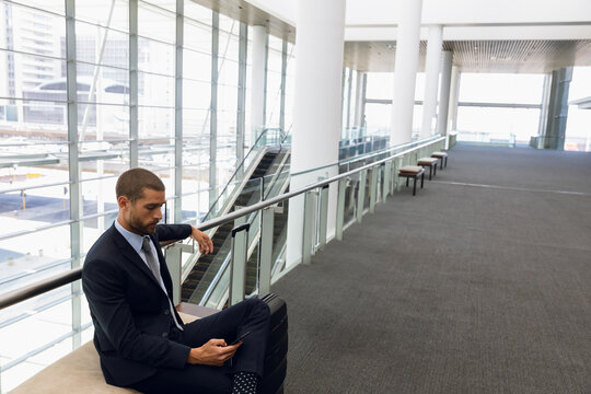 Businessman in suit checking smartphone while waiting in modern conference center, copy space