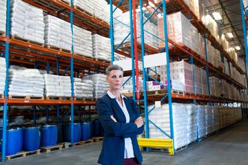 Confident businesswoman standing in large warehouse, surrounded by stocked shelves, copy space