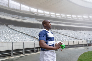 Rugby player holding ball in empty stadium, focused and determined