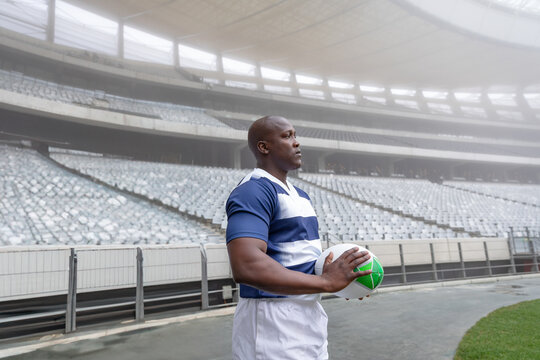 Rugby player holding ball in empty stadium, focused and determined