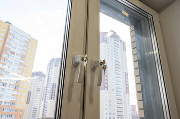 Obraz premium A close-up of a white window with keys in the handles, overlooking buildings