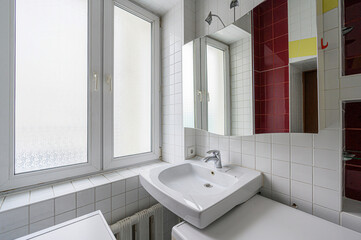 A bright bathroom features a white sink, tiled walls and a window. A mirror reflects the window and the wall