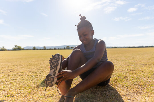 Fototapeta African American girl tying shoelaces on field, preparing for outdoor activity