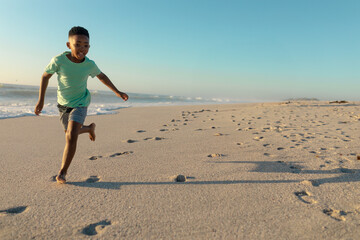 African American boy running joyfully on sandy beach at sunset, copy space
