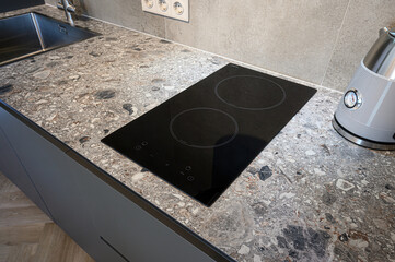 A kitchen countertop features a black induction cooktop, a kettle, and a sink. The countertop has a...