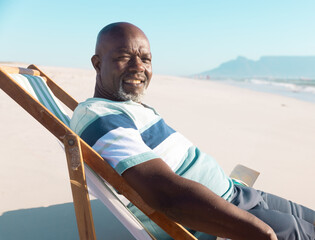 Relaxing on beach, senior man smiling while sitting in deck chair by ocean