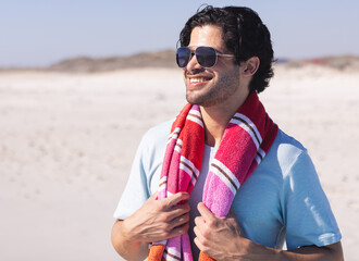 Smiling man with sunglasses enjoying sunny day at beach with towel