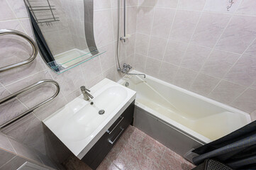 A bathroom featuring a sink vanity, a bathtub with a shower, and light-colored tiled walls. A mirror and towel rack complete the space.
