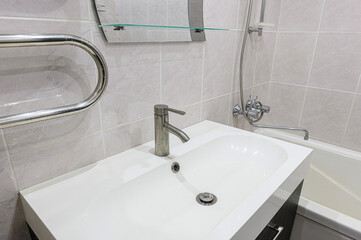 A bathroom sink area with a white countertop, silver faucet, and beige tiled wall. Mirror and towel warmer visible