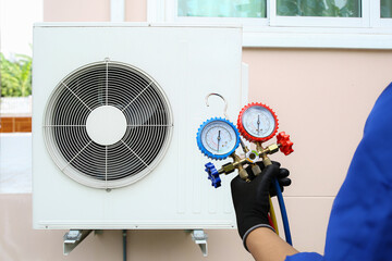 Air conditioning electrical technician using manifold gauge measuring tool checking refrigerant pump filling home air conditioner and maintenance heat fix repair and clean outdoor compressor unit.