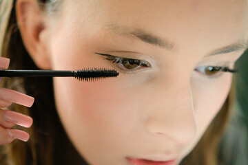 Obraz premium A beautiful teenage girl applying mascara to her eyelashes in a close-up shot. Self-applied makeup highlighting youthful style and confident grooming.