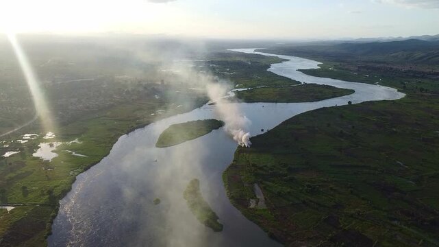 Aerial view of the nile river winding through lush green landscapes with sunlight and smoke trails visible