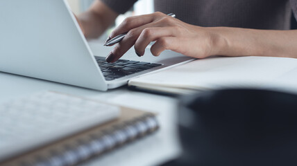 Close up of business woman working on laptop, searching the information and writing on notebook,...