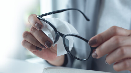 Person and cleaning vision glasses with paper wipes for lens protection, sight and eye care safety at office. Closeup.  Business woman wipes dirt on clear spectacle frames © tippapatt