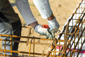 
Close-up of worker's hands in gloves, who is tying reinforcement for foundation reinforcement.
