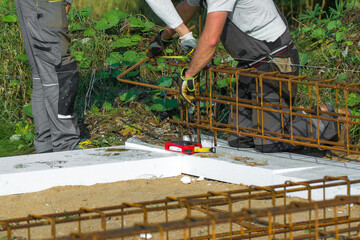 
Close-up of worker's hands in gloves, who is tying reinforcement for foundation reinforcement.
