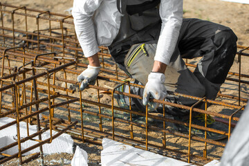 
Close-up of worker's hands in gloves, who is tying reinforcement for foundation reinforcement.
