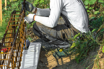 
Close-up of worker's hands in gloves, who is tying reinforcement for foundation reinforcement.

