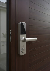 Modern dark brown wood door with a sleek silver digital lock mechanism. Close-up view of the door handle and integrated keypad. Home security and smart home technology.