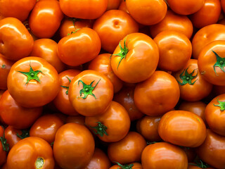 A full frame, close-up shot of a large pile of fresh red and orange tomatoes, highlighting their vibrant color, smooth texture, and green stems. Perfect for food and fresh produce concepts.