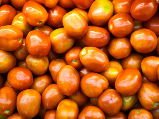 A full frame, close-up shot of a large pile of fresh red and orange tomatoes, highlighting their vibrant color, smooth texture, and green stems. Perfect for food and fresh produce concepts.