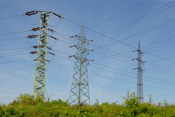 Power transmission towers standing tall against a clear blue sky, surrounded by greenery.