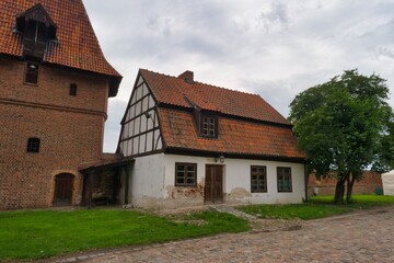 Historic half timbered house stands near brick tower in a rural setting on a cloudy day in Germany