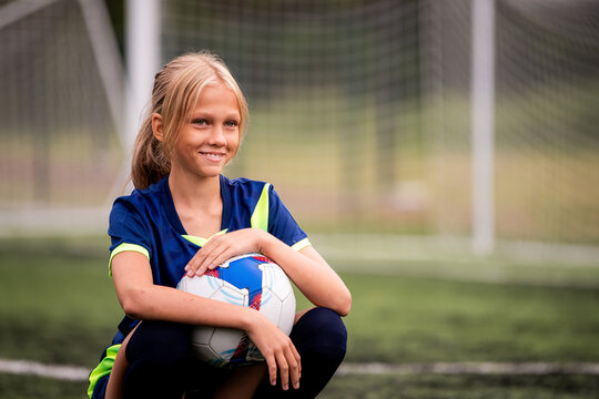 girl player in sport uniform with football ball on green grass field.