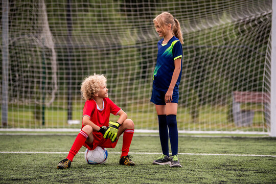 Boy and girl football players communicate on a green field.