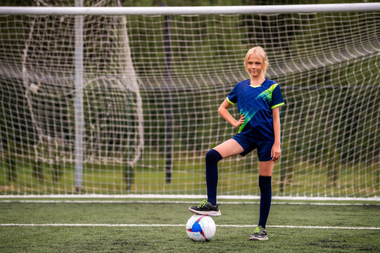 Girl with soccer ball in front of net on green soccer field.