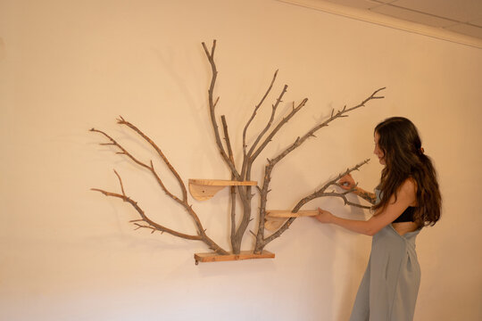 Woman installing original wooden tree-shaped shelf on wall