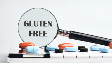 GLUTEN FREE words written through a magnifying glass on a calculator with tablets on a gray background. The concept of medicine
