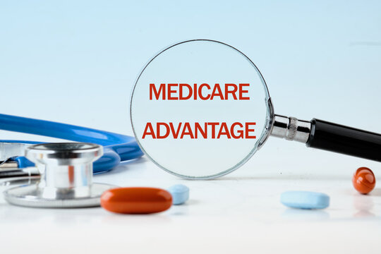 Medical and health concept. Phrase MEDICARE ADVANTAGE written through a magnifying glass on a blue background. Concept photo