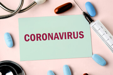 Health and medical concept. Concept word CORONAVIRUS on the business card in a composition with a stethoscope, pills and a syringe.