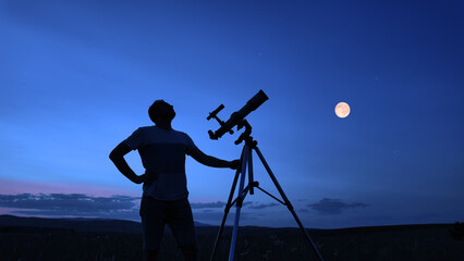 Amateur astronomer using telescope for watching stars, Moon, planets and other celestial objects from a field in nature.
