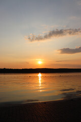 A stunning, vibrant sunset over a calm lake, with the sun's golden light reflecting on the water's surface and silhouetting the distant shoreline.