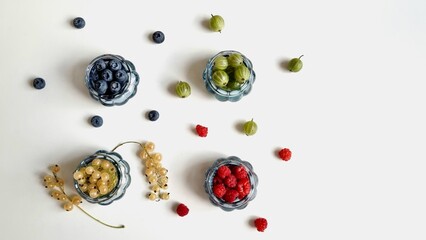 concept of proper nutrition and diets, blue glass vases with raspberries, currants, blueberries and gooseberries on a white background.