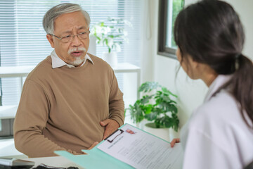 Doctor Reviewing Medical File While Interviewing Elderly Patient at Clinic or Hospital