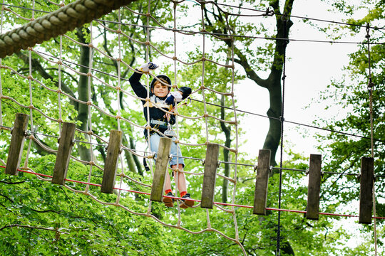 School boy in forest adventure park. Acitve child, kid in helmet climbs on high rope trail. Agility skills and climbing outdoor amusement center for children. Outdoors activity for kid and families.