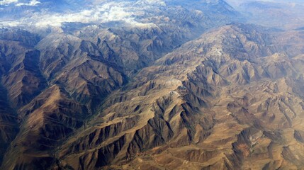 Obraz premium Aerial View of Rugged Mountain Range with Dramatic Peaks and Atmospheric Clouds, Ideal for Travel and Adventure Imagery