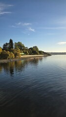 Obraz premium Bright view of Lago Ranco on a sunny day with blue skies, sparkling waters, and surrounding mountains, showcasing the natural beauty of southern Chile.