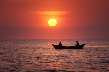 Silhouette of two figures in a small boat at sunset