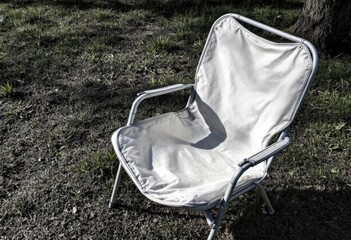 A light grey canvas folding chair sits on patchy grass in dappled shade, suggesting outdoor leisure or temporary rest
