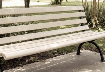 Off-white park bench with horizontal slats, curved ends, and black metal supports, situated on a paved area near greenery