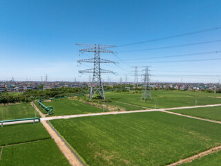 Power transmission towers stand in a vast green field under a clear sky.