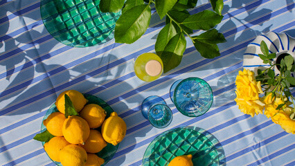 On a sunlit striped tablecloth, lemons bask amidst azure glassware, evoking Midsummer feasts and...