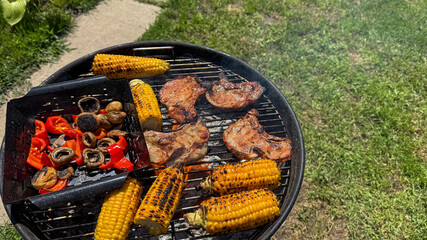 Grilled corn and sizzling meats on a charcoal barbecue evoke National Barbecue Month and midsummer culinary bliss